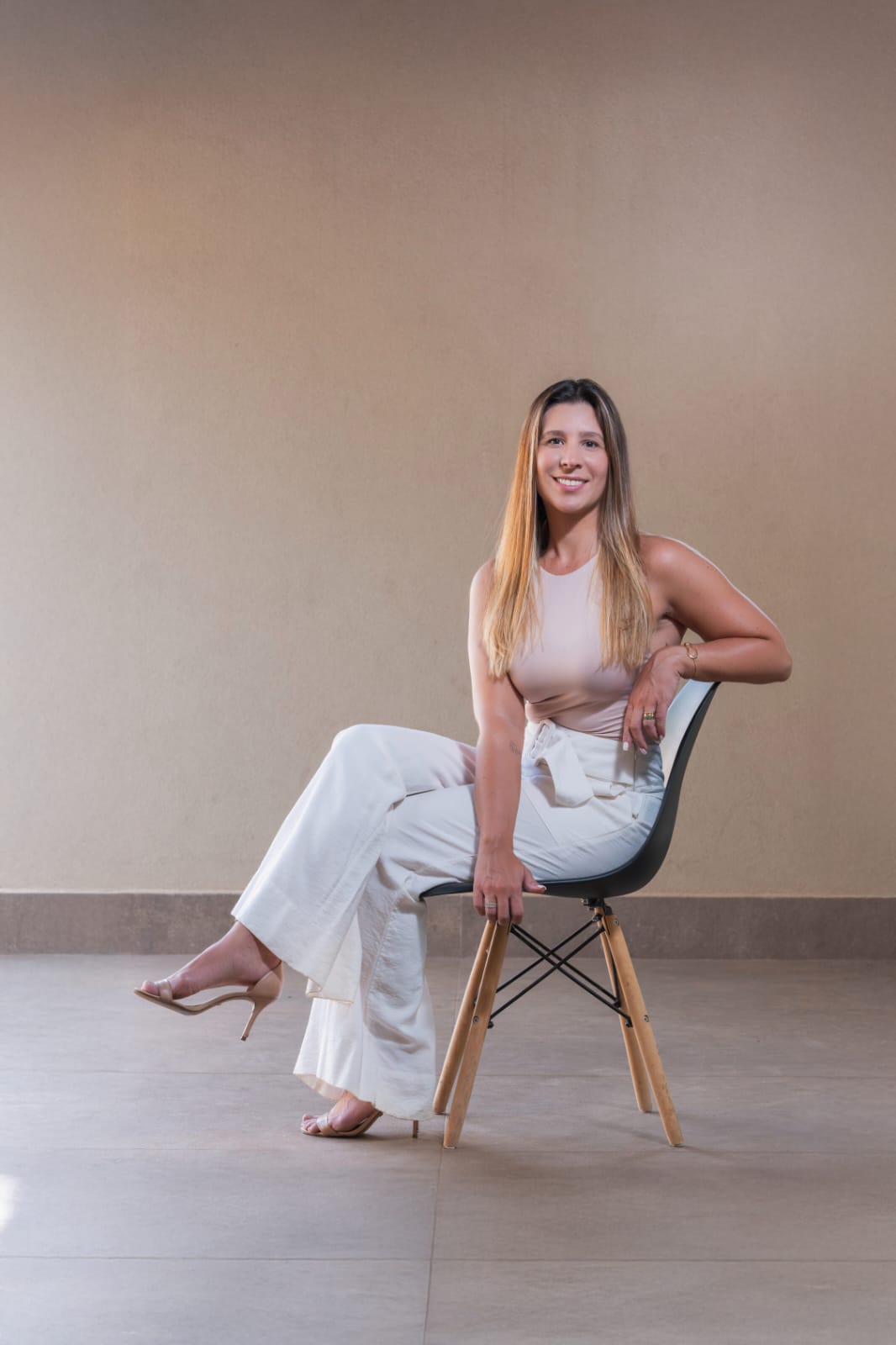 Renata Hamu sentada em uma cadeira, de corpo inteiro, com roupa clara
